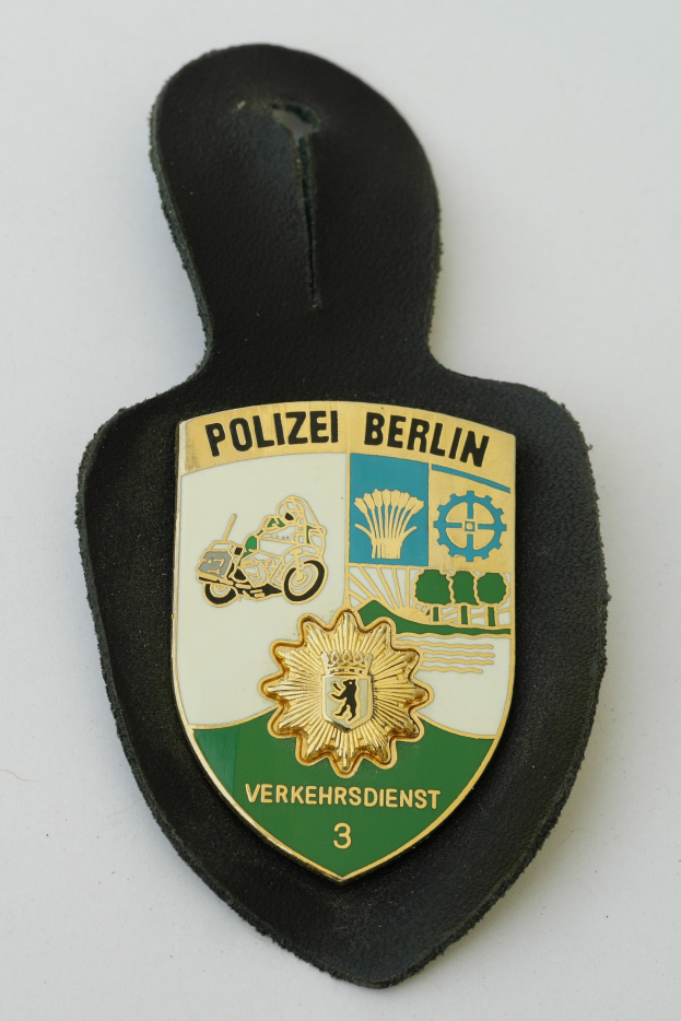 Ein schildförmiges Polizeibadgebilde mit "Polizei Berlin" in fetter schwarzer Schrift auf einem blauen Hintergrund mit einem weißen Stern und Rahmen, das auf einer Oberfläche ruht.