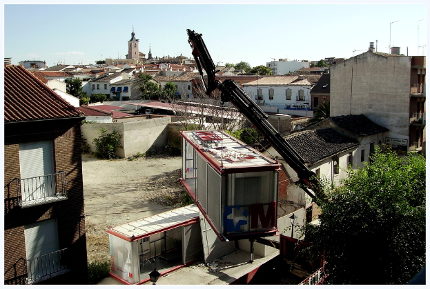 Eine Stadtansicht mit zahlreichen Gebäuden, Bäumen und einem Kran mit einem Container.
