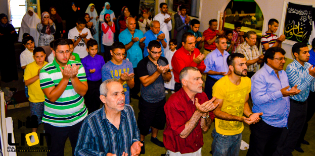 Menschen beten in einem Saal, mit Text in der linken unteren Ecke.