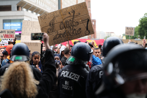 Gruppe von Menschen mit Helmen und Schildern bei einer Demonstration vor einem Gebäude