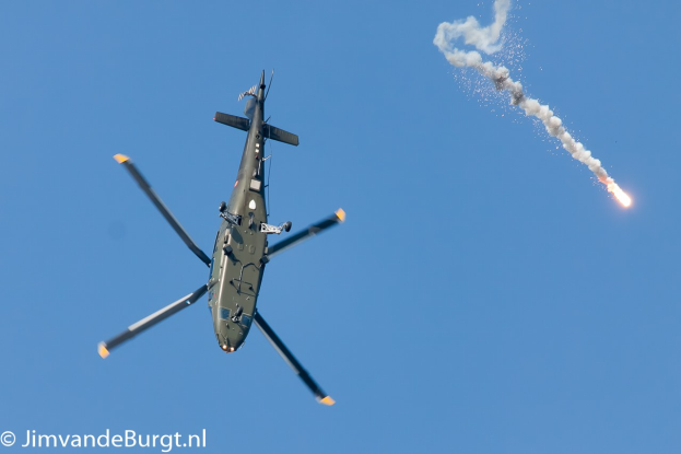 Militärhubschrauber steigt mit einem rauch- und feuerabgebenden Missile auf, Text in der unteren linken Ecke.