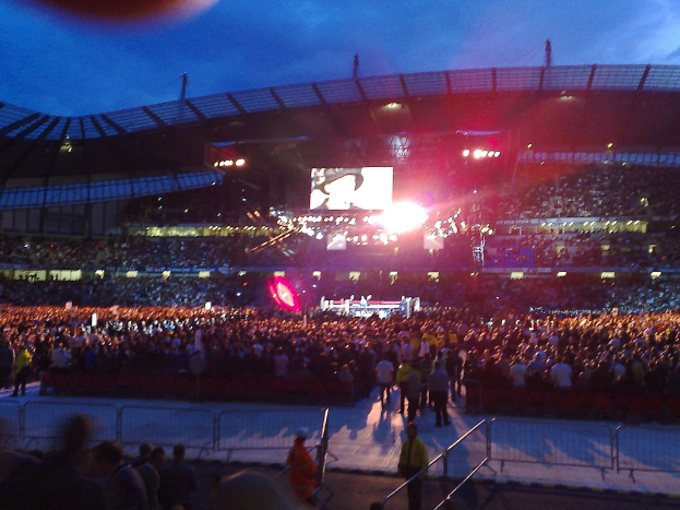 Ein Konzertort mit Menschen, Bühnenlichtern und einem Projektionsschirm.