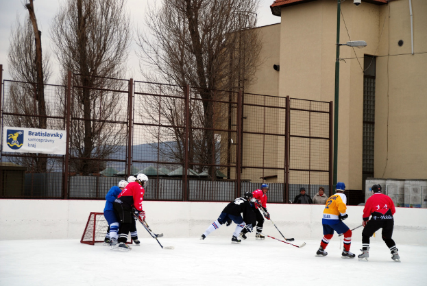 Menschen, die auf einem Eisstadion mit Gebäuden, Bäumen, einer Straßenlaterne, einem Namensschild und Zäunen im Hintergrund unter einem Himmel Eis Hockey spielen.