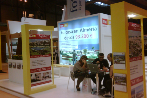 Eine Gruppe von Menschen sitzt um einen Tisch, schaut auf einen Laptop und hat mehrere Flyer mit verschiedenen Anzeigen daneben.