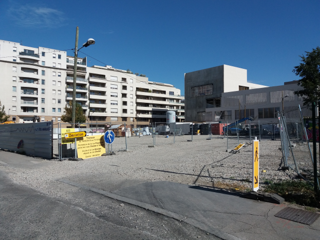 Eine Baustelle mit verschiedenen Geräten, darunter Pfosten, Schilder, ein Zaun, ein Straßenpfosten, Bäume, Fahrzeuge, Gebäude mit Fenstern und einem bewölkten Himmel.