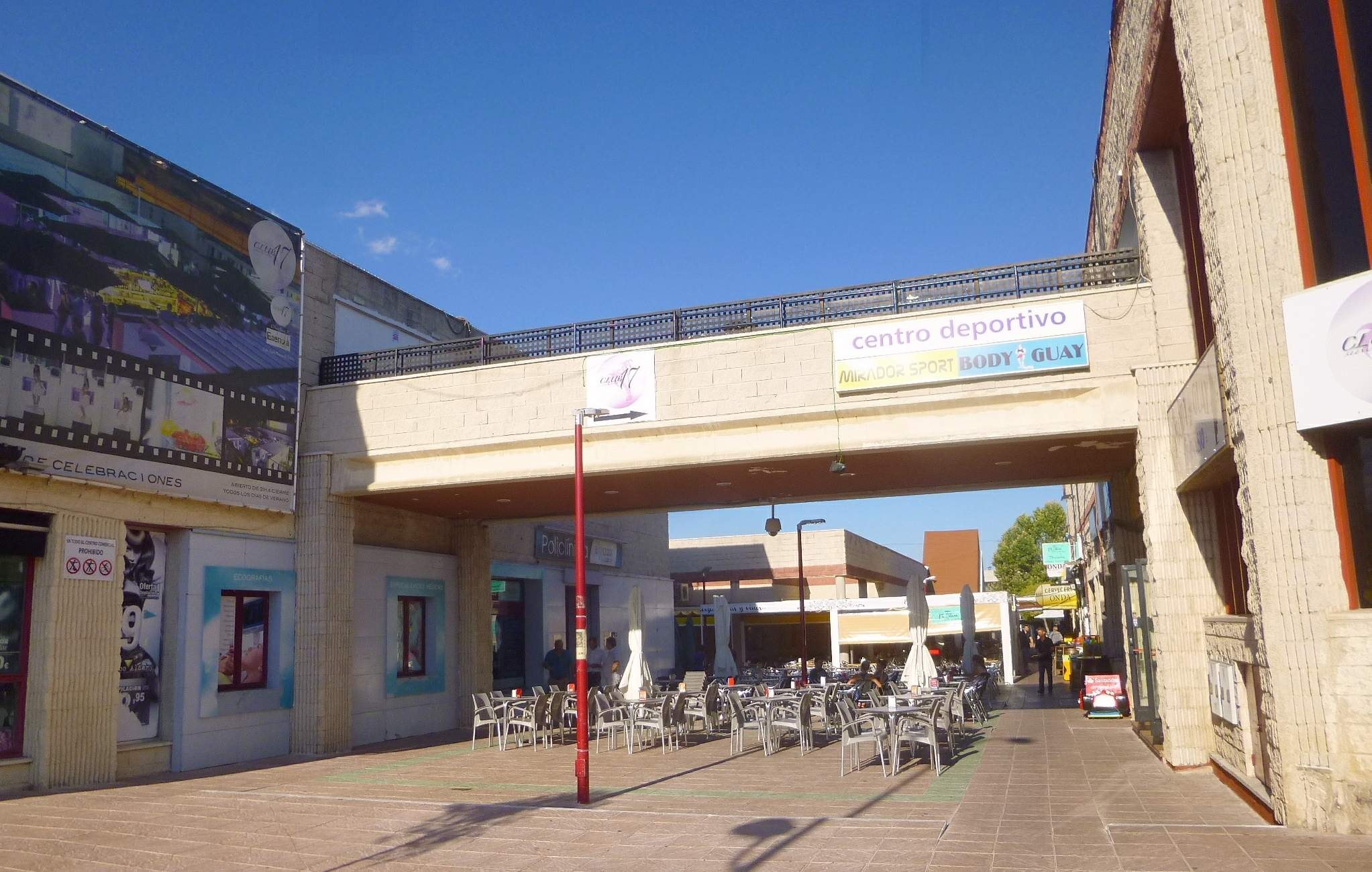 Ein belebter Stadtplatz mit Außensitzgelegenheiten, Straßeneinrichtungsgegenständen, Bäumen und einer bewölkten Himmel.