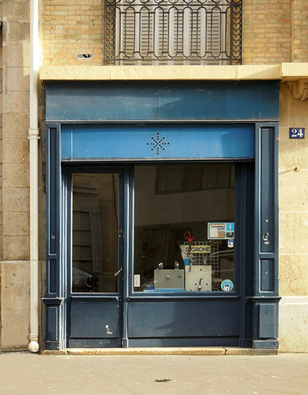 Blaue Tür und Fenster an einem Gebäude mit einem Rohr an der Wand, einem Geländer oben und einer Straße unten.