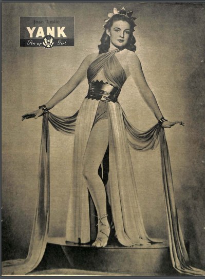 Ein Schwarz-Weiß-Foto von Schauspielerin Joan Leslie, die auf einer Bühne in einem langen, hochgeschlossenen Kleid mit langen Ärmeln steht, ihr Haar im Stil der 1940er Jahre frisiert und die Augen geschlossen in einer friedlichen Pose, mit ihrem Namen oben im Rahmen.