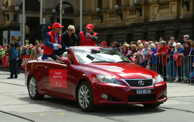 Menschen fahren in einem Auto auf einer Straße mit verschiedenen Objekten, Schildern und Menschen im Hintergrund.