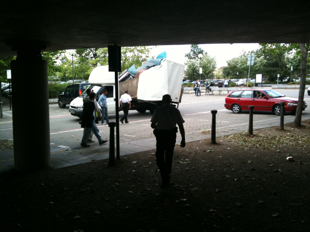 Eine belebte Straßenszene mit zahlreichen Fußgängern, einem Auto und einem Lastwagen.