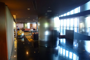 Eine geräumige First-Class-Lounge am Hong Kong International Airport mit großen Fenstern, hohen Decken mit elektrischem Licht, Sitzgelegenheiten wie Stühle und Sofas, Tischen, einem Teppichboden und einer mittigen Säule.