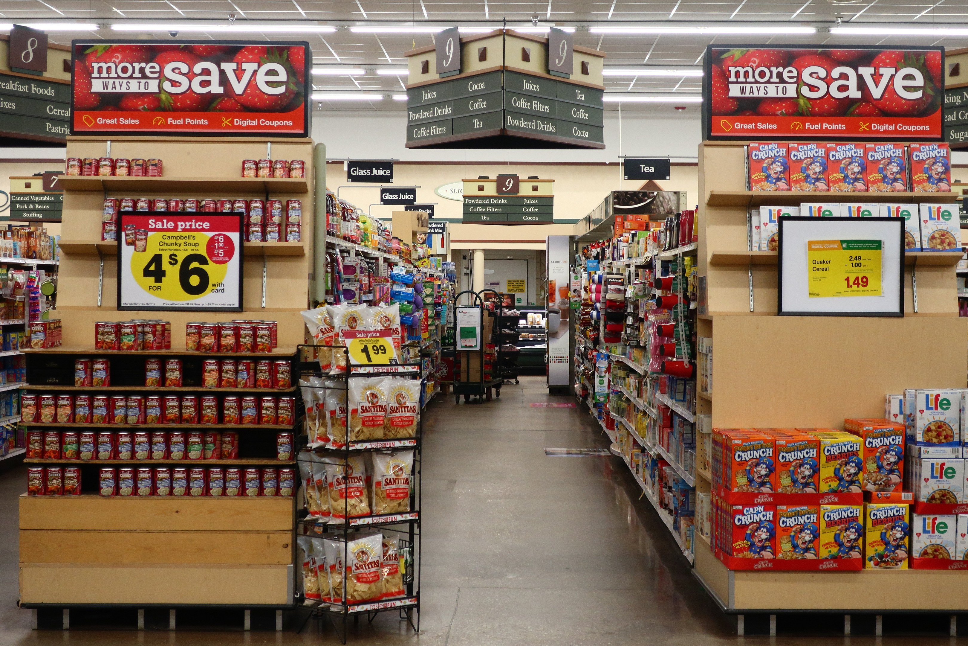 Ein Convenience-Store-Interieur mit Regalen und Bodenbestand an verschiedenen Lebensmitteln, beleuchtet von Deckenlampen und mit Informationsschildern.