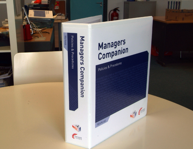 Ein Buch auf einem Tisch mit einem Stuhl dahinter, in der Nähe einer Tür, Feuerlöscher, Dateien und anderen Gegenständen.